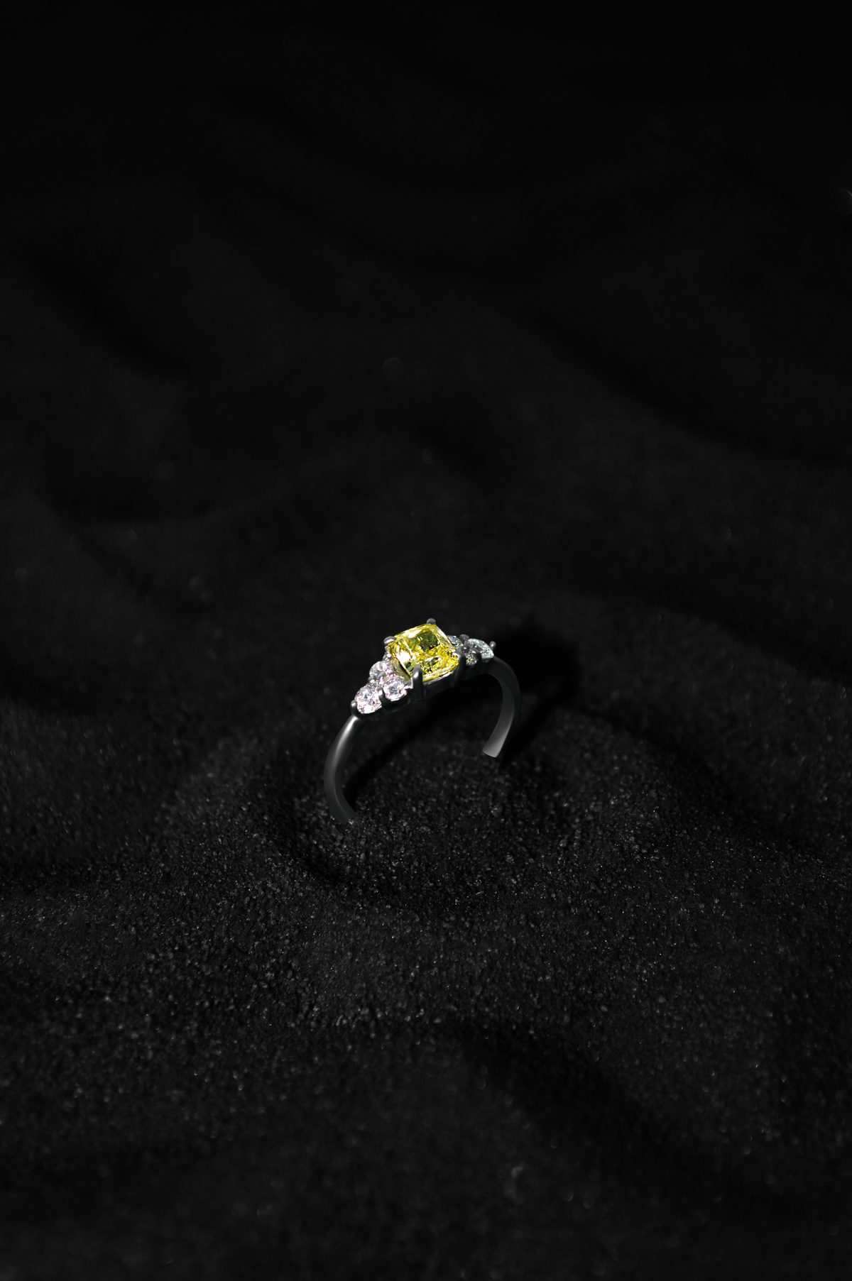 Anillo YS.03 de tres piedras con diamante amarillo central y diamantes blancos laterales en oro blanco 14k, sobre arena negra